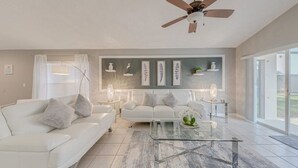A modern living room with a white sofa, a glass coffee table, and a ceiling fan.