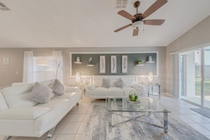 A modern living room with a white sofa, a glass coffee table, and a ceiling fan.