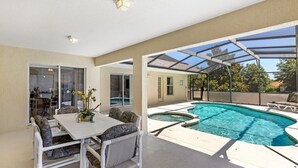 Un espace extérieur abrité comprenant une piscine, une table à manger avec des chaises et une véranda fermée par des baies vitrées.