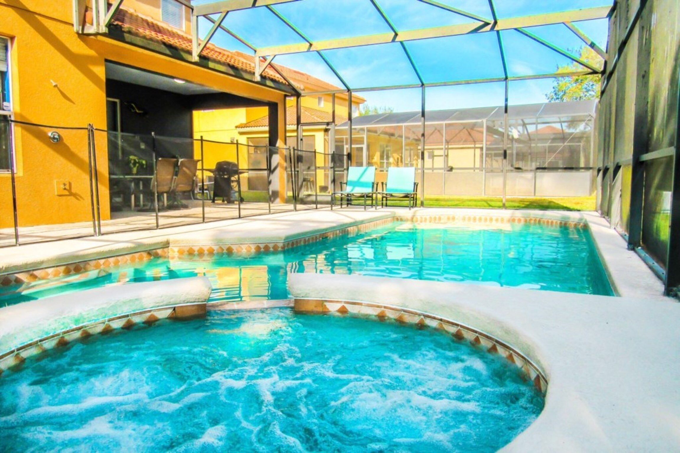 A swimming pool with a glass enclosure, surrounded by a patio area with chairs and a table.
