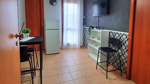 A compact kitchen with a dining area, a TV mounted on the wall, and a ceiling fan. - Black Suite With Terrace, sea View Located in the Center (Margherita di Savoia)