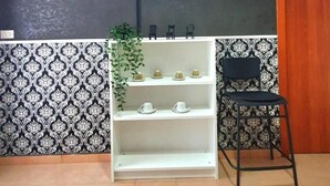 A room with a television mounted on the wall, a white shelf with decorative items, a black chair, and patterned wallpaper. - Black Suite With Terrace, sea View Located in the Center (Margherita di Savoia)