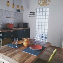 Un comedor con una mesa de madera, sillas, una cocina al fondo y una ventana con vistas.
