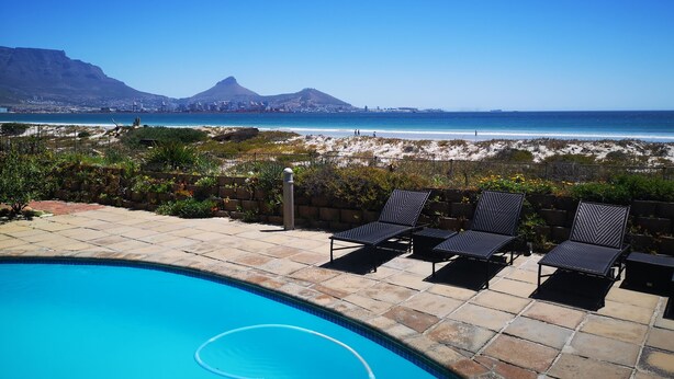 A pool area with lounge chairs and a view of the beach and mountains. - Family Cape Town Beachfront Apartment (Cape Town)