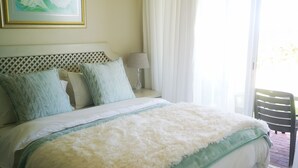A bedroom with a bed, a nightstand, a lamp, a window with curtains, and a framed picture on the wall. - Family Cape Town Beachfront Apartment (Cape Town)