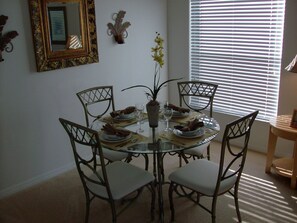Enjoy meals in this dining area with a round table and six chairs, surrounded by a decorative plant and a large window.