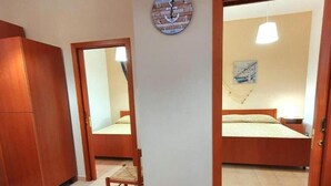 A room with a bed, a wooden wardrobe, a chair, a wall clock, and a painting. - Splendid Quadruple Room Located 2 Steps From the sea (Margherita di Savoia)