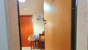 A hallway with a wooden door, a dining area with a table and chairs, and a mat on the floor that reads "HOME Sweet HOME". - Splendid Quadruple Room Located 2 Steps From the sea (Margherita di Savoia)