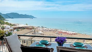 A terrace with a view of the beach and sea, tables with blue plates, and a chair with a cushion.