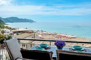 A terrace with a view of the beach and sea, tables with blue plates, and a chair with a cushion. - Corfu Glyfada Menigos 150 (Corfu)
