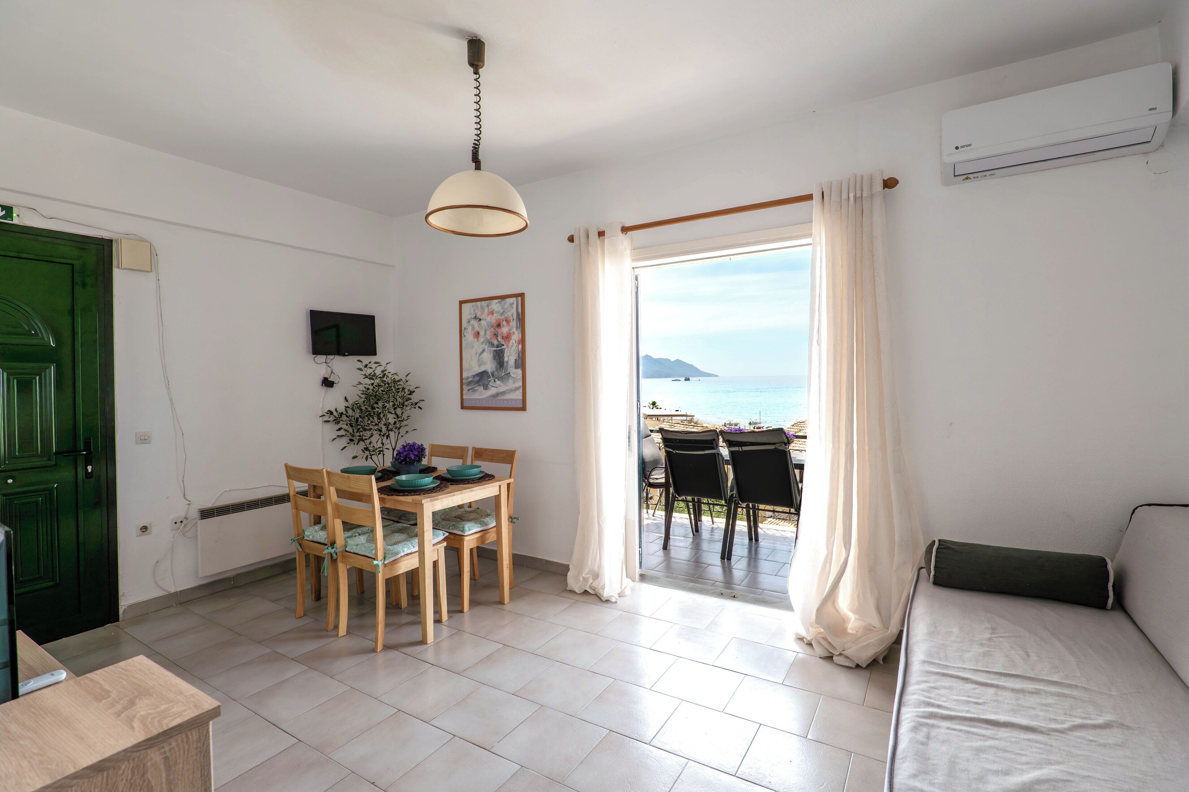 Una habitación con zona de comedor, sofá, televisor y vista al mar.