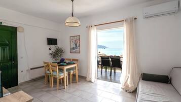 Una habitación con zona de comedor, sofá, televisor y vista al mar.
