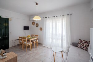 Una habitación con una mesa de comedor, sillas, un sofá, un televisor y un ventanal con cortinas.