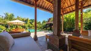 Un espace extérieur abrité, aménagé avec des meubles en bois, des plantes tropicales et une piscine.