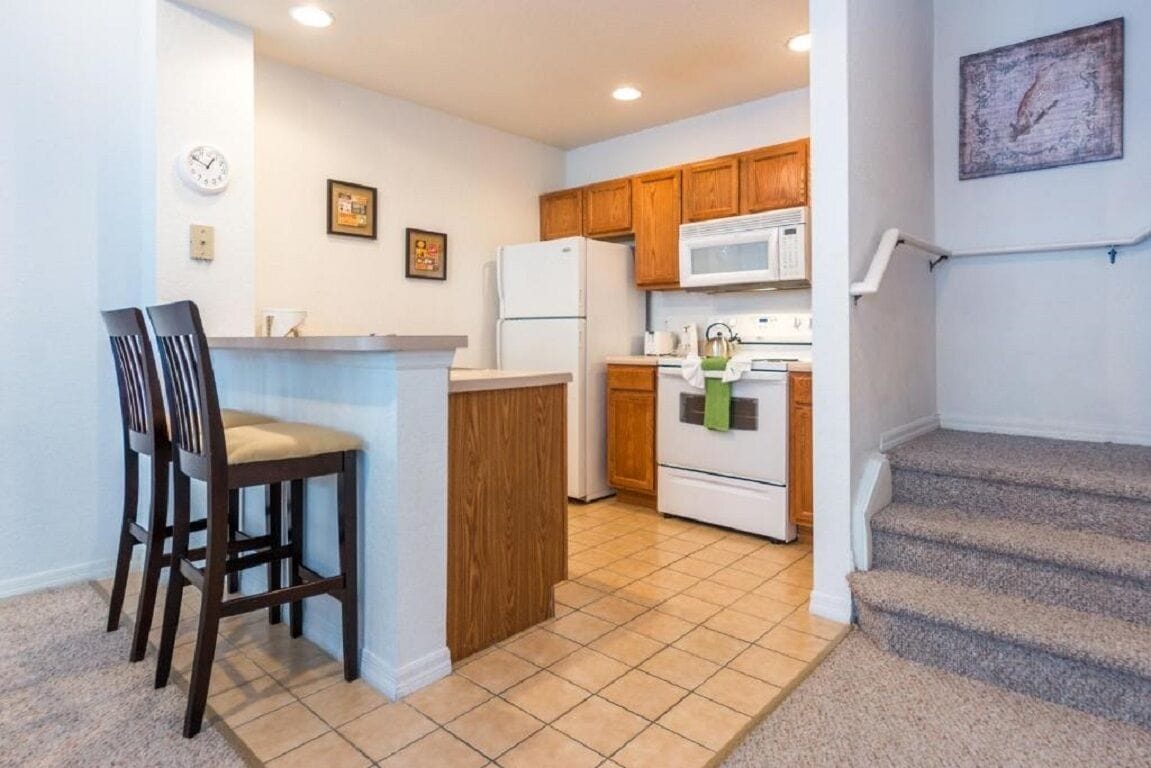 A kitchen with wooden cabinets, a microwave, a refrigerator, and a small island with chairs.