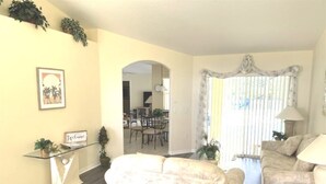 A living room with a beige sofa, a glass coffee table, and a lamp. There is a dining area visible through an archway. - 4 Bedroom Budget Home and Private Pool (Davenport)
