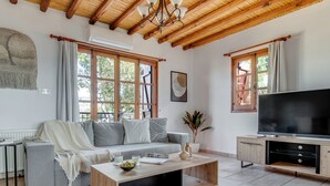 Ein modernes Wohnzimmer mit einer Couch, einem Couchtisch, einem Fernseher und großen Fenstern.