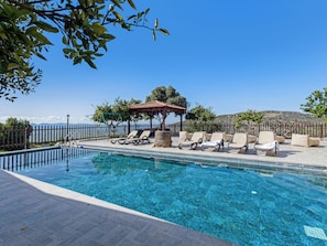 A clear blue pool with lounge chairs and a gazebo.