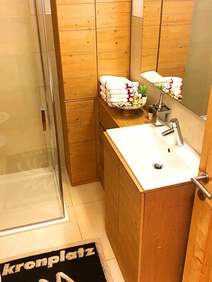 A modern bathroom with a glass shower enclosure, wooden cabinetry, a white sink, and a mirror. - Apartment on the ski Slopes at Plan de Corones (Valdaora)