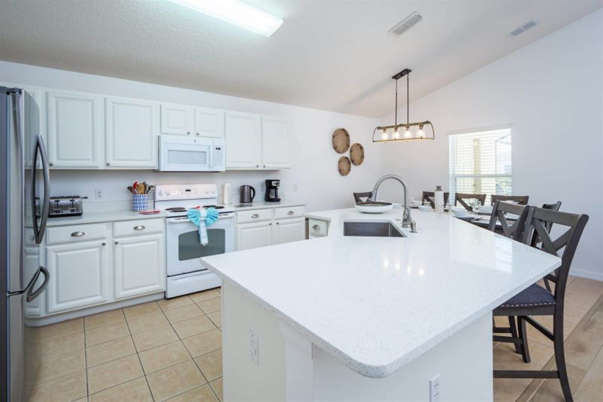 A modern kitchen with white cabinets, a central island, and a dining area with chairs.