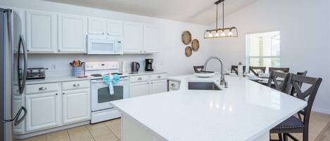 A modern kitchen with white cabinets, a central island, and a dining area with chairs.