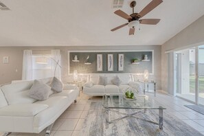 A modern living room with a white sofa, a glass coffee table, and a ceiling fan.