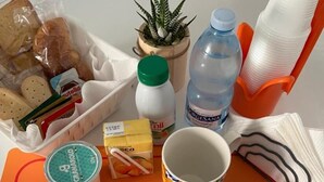 A table with a placemat labeled "Cappuccino Briosches," containing food items, a small plant, a water bottle, a mug, and cutlery. - Room-holiday House the Zagare (Palagiano)