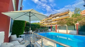 A swimming pool with a glass barrier, outdoor seating, and a large umbrella. - Corfu Dream Holidays Villa Kanoni (Corfu)