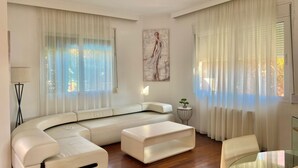 A modern living room with a curved white sofa, a glass coffee table, and a glass dining table. - Corfu Dream Holidays Villa Kanoni (Corfu)