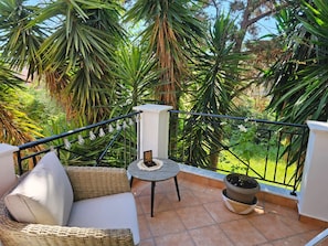 Relax on the balcony with a wicker sofa, small table, and potted plant amidst lush greenery views.