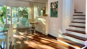 A spacious living area with a wooden staircase, a dining area with a glass door leading to a balcony, and a kitchen visible through a glass partition. - Corfu Dream Holidays Villa Kanoni (Corfu)