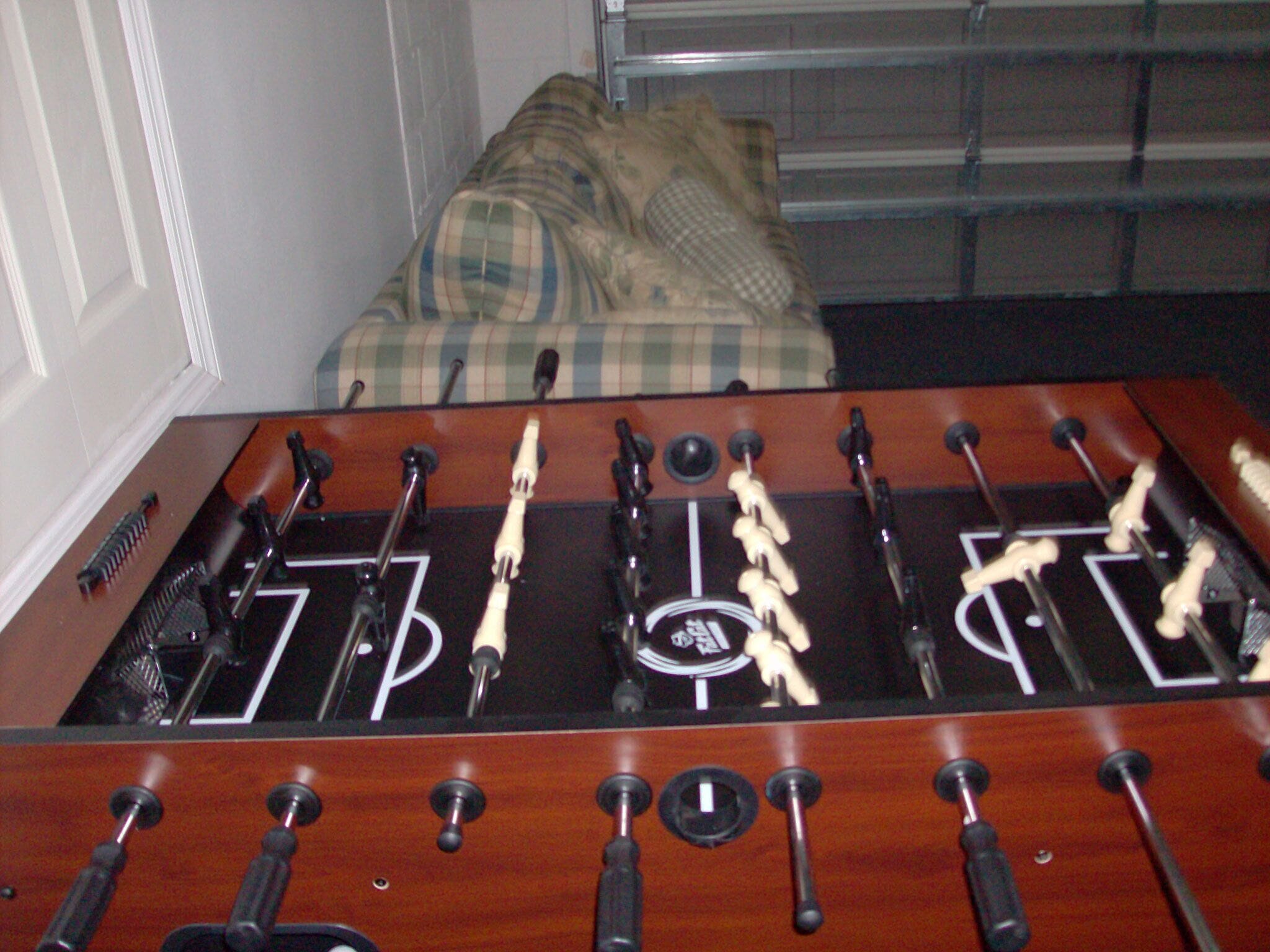 A foosball table in a room with a plaid-patterned couch in the background.