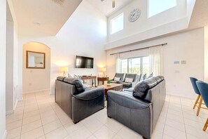 A spacious living room with a high ceiling, a flat-screen TV, and a large window with curtains. - 5 Bedroom Executive Pool Home and Games Room (Davenport)