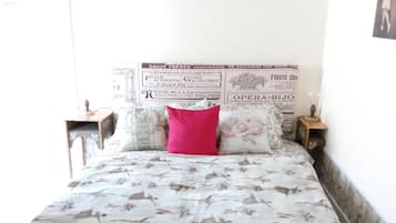A bed with floral bedding, a red pillow, and a wall with vintage posters.