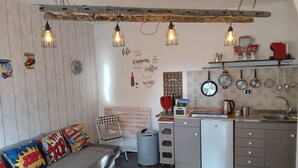 A compact kitchen with a wooden ceiling, a sofa with colorful cushions, and a wall with a coffee-themed sign. - Casa Carolina A Bit Different (Pennadomo)