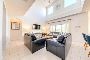 A spacious living room with a high ceiling, a flat-screen TV, and a large window with curtains. - 5 Bedroom Executive Pool Home With Games Room (Davenport)
