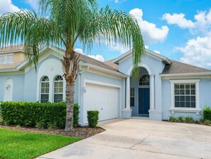 Traditional home with a central entrance, flanked by garage doors, set amidst a well-manicured lawn and a mature palm tree.