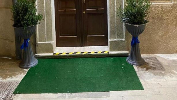 A hotel entrance with a double wooden door, a green mat, and two potted plants. - Beautiful Family Apartment in the Center (Margherita di Savoia)