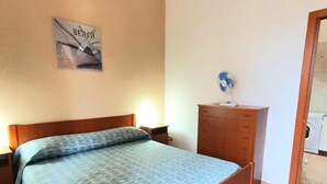 A bedroom with a bed, wooden dresser, and a wall-mounted light fixture. - Beautiful Family Apartment in the Center (Margherita di Savoia)