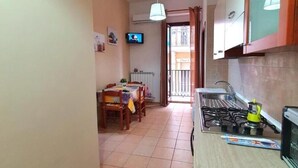 A narrow kitchen with a tiled floor, a dining area with a table and chairs, a clock on the wall, and a television on the wall. - Beautiful Family Apartment in the Center (Margherita di Savoia)