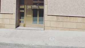 Une entrée d’immeuble avec une façade recouverte de carreaux, un toit en métal et une porte dotée d’un panneau de verre.
