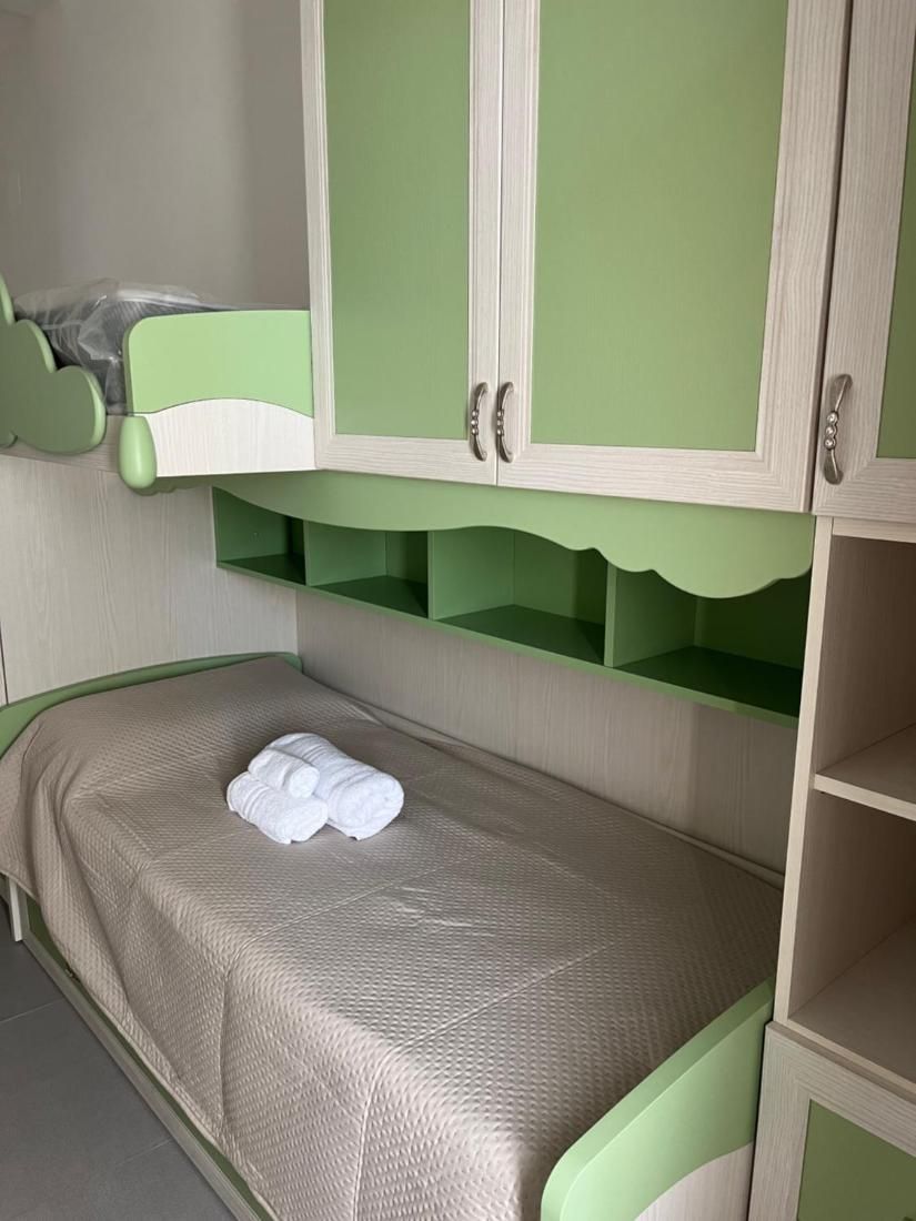 Un lit superposé avec une tête de lit verte et un lit simple en dessous. Le lit superposé est doté de deux rangées de tiroirs, et le lit simple a une étagère.