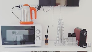 Une cuisine équipée d’un four à micro-ondes, d’une bouilloire et d’une machine à café, le tout posé sur un plan de travail blanc.