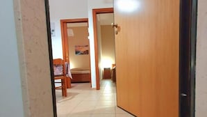 A hallway with a wooden door, a tiled floor, and a 'Home Sweet Home' mat at the entrance. - Splendid Quadruple in the Center, 2 Steps From the sea (Margherita di Savoia)