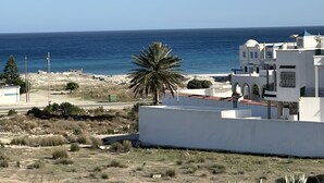 A coastal view with a clear sky, a sandy beach, and white buildings with blue roofs.