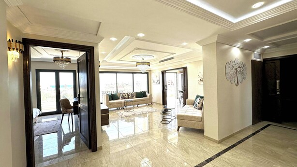 A spacious living area with a high ceiling, a chandelier, and a large window offering a view of the outdoors.