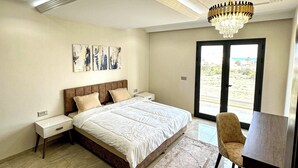 A bedroom with a large bed, bedside tables, a chandelier, a desk, and a view through a window.
