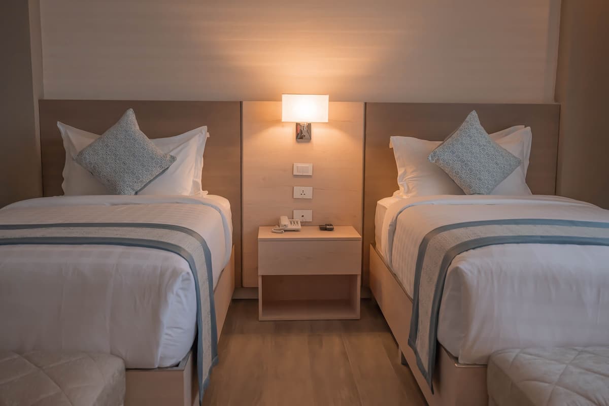 Une chambre d’hôtel avec deux lits, une table de chevet avec une lampe et une petite étagère.