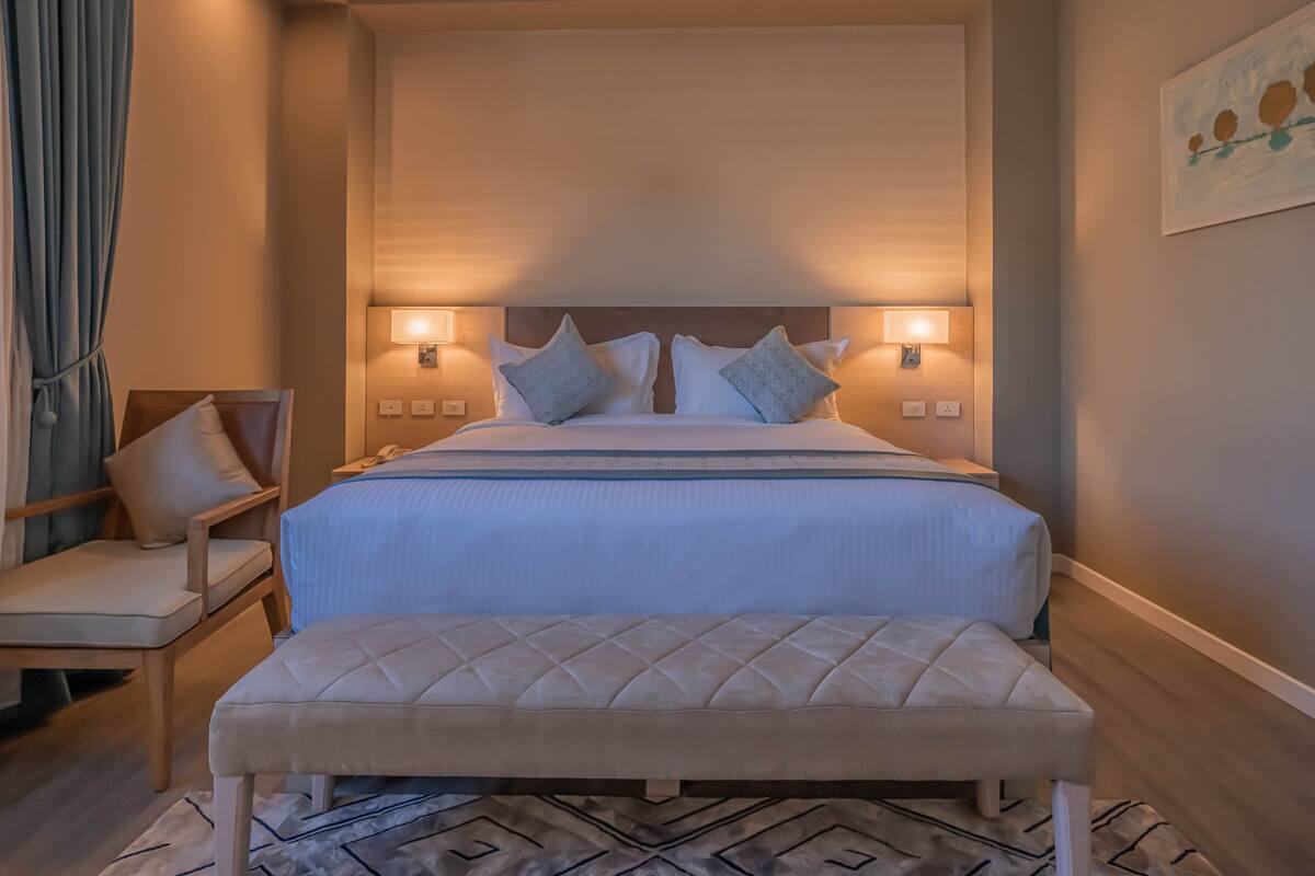 Une chambre d’hôtel avec un grand lit, deux lampes de chevet, une tête de lit en bois et un banc.