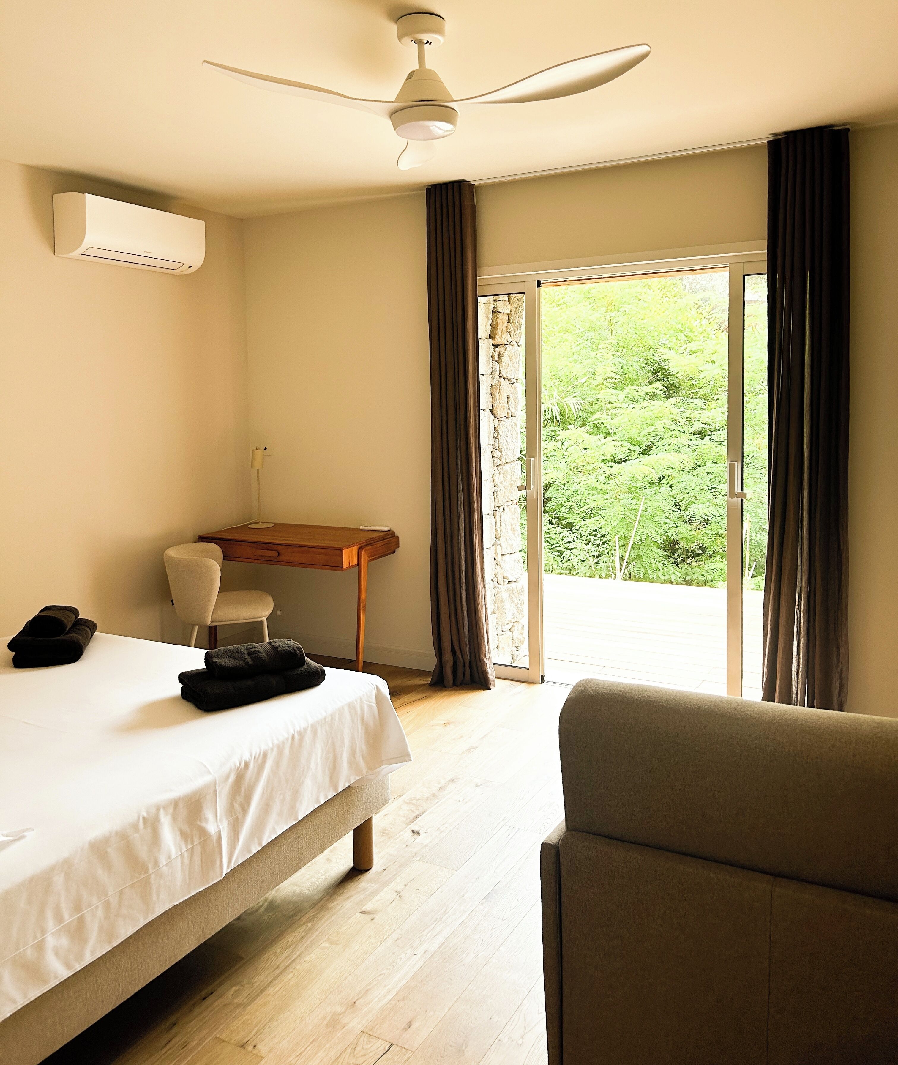 Een hotelkamer met een bed, een bureau, een stoel en uitzicht op groen door het raam.